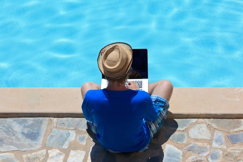 プール沿いでパソコンを操作している男性の画像